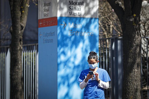 A medical worker uses her phone while wearing a surgical mask outside Mt. Sinai West, Thursday, March 26, 2020, in New York. The new coronavirus causes mild or moderate symptoms for most people, but for some, especially older adults and people with existing health problems, it can cause more severe illness or death. (AP Photo/John Minchillo)