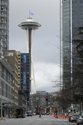 A lone pedestrian crosses an empty street as a flag that reads &quot;#We Got This Seattle&quot; flies on the roof of the Space Needle, Thursday, March 26, 2020, in Seattle. The flag was raised by Mayor Jenny Durkan Thursday, who said it is intended to be a symbol of unity and encouragement as the city faces a state-wide stay-at-home mandate and one of the worst outbreaks of the new coronavirus in the U.S. (AP Photo/Ted S. Warren)