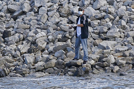 A fisherman observes social distancing while wearing a face mask as he prepares to cast his line Wednesday afternoon, March 25, 2020, at the Ross Barnett Reservoir spillway, near Brandon, Miss. Residents are taking advantage of warm weather in the outdoors and maintain social distancing as they fish. (AP Photo/Rogelio V. Solis)