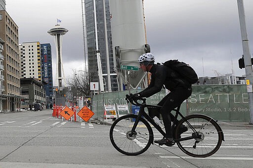 A cyclist rides on an empty street as a flag that reads &quot;#We Got This Seattle&quot; flies on the roof of the Space Needle, Thursday, March 26, 2020, in Seattle. The flag was raised by Mayor Jenny Durkan Thursday, who said it is intended to be a symbol of unity and encouragement as the city faces a state-wide stay-at-home mandate and one of the worst outbreaks of the new coronavirus in the U.S. (AP Photo/Ted S. Warren)