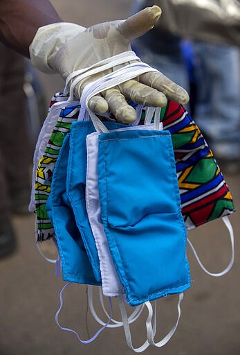 A street vendor wearing surgical glove, to protect against coronavirus, sells face musks at a minibus taxi station in Johannesburg, South Africa, Thursday, March 26, 2020.  South Africa goes into a nationwide lockdown for 21 days in a few hours, in an effort to mitigate the spread to the coronavirus.  (AP Photo/Themba Hadebe)