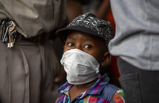 A young boy wearing a face mask to protect against coronavirus, with his father stands in a queue to shop in Soweto, South Africa, Thursday, March 26, 2020. In hours South Africa goes into a nationwide lockdown for 21-days in an effort to mitigate the spread to the coronavirus.  (AP Photo/Themba Hadebe)