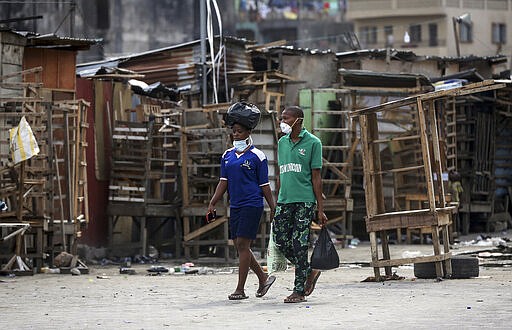 People wearing face masks walk past closed street stalls and shops due to a government ban on the operation of non-essential businesses and markets to halt the spread of the new coronavirus, in Lagos, Nigeria Thursday, March 26, 2020.  (AP Photo/Sunday Alamba)