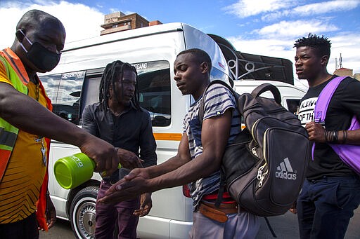 Jacob Maphala, a taxi marshal wearing a face mask, sprays sanitizer to passengers to protect against coronavirus, at a minibus taxi station in Johannesburg, South Africa, Thursday, March 26, 2020. It is just hours before South Africa goes into a nationwide lockdown for 21-days in an effort to mitigate the spread to the coronavirus. (AP Photo/Themba Hadebe)