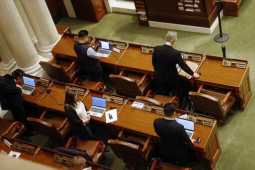 Lawmakers in the Minnesota House practice social distancing during prayer by the chaplain Thursday, March 26, 2020 at the State Capitol in St. Paul, Minn. as they met to take up bills related to the coronavirus in the state. A limited number of members were allowed on the House floor. The new coronavirus causes mild or moderate symptoms for most people, but for some, especially older adults and people with existing health problems, it can cause more severe illness or death. (AP Photo/Jim Mone)