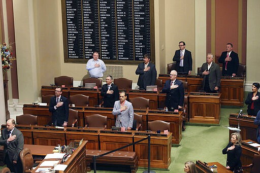 Lawmakers doing social distancing in the Minnesota House take the Pledge of Allegiance, Thursday, March 26, 2020 at the State Capitol in St. Paul, Minn. before the body met to take up bills related to the coronavirus in the state. A limited number of members were allowed on the House floor. The new coronavirus causes mild or moderate symptoms for most people, but for some, especially older adults and people with existing health problems, it can cause more severe illness or death. (AP Photo/Jim Mone)