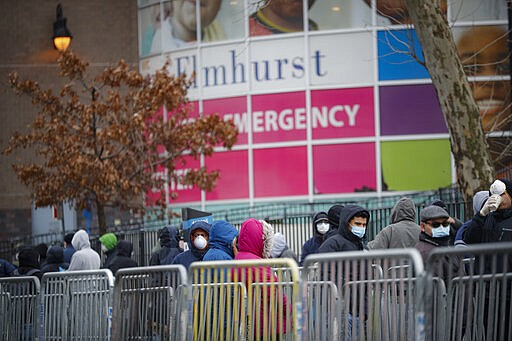 In this March 25, 2020 photo, patients wear personal protective equipment while maintaining social distancing as they wait in line for a COVID-19 test at Elmhurst Hospital Center in New York.  (AP Photo/John Minchillo)