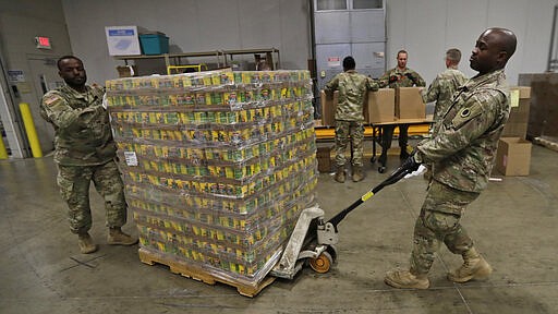 Ohio National Guard Specialist Scott Eubanks, right, and Corp. Tommie Davis move a skid of peaches to prepare for repackaging emergency food boxes for food distribution at the Cleveland Food Bank, Tuesday, March 24, 2020, in Cleveland. (AP Photo/Tony Dejak)