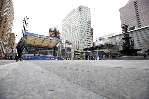 In this Tuesday, March 24, 2020 photo, a woman walks across Fountain Square  in Cincinnati, on the first day of Ohio Gov. Mike DeWine's shelter-in-place order in response to the new coronavirus pandemic. All non-essential businesses are closed and residents have been asked to stay at home. (Kareem Elgazzar/The Cincinnati Enquirer via AP)