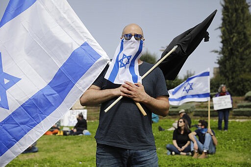 Israelis hold national flags during a protest against Prime Minister Benjamin Netanyahu outside the national parliament in Jerusalem, Monday, March 23, 2020. The opposition has accused Netanyahu of using the coronavirus crisis as cover to undermine the country's democratic institutions. With the country in near-shutdown mode, Netanyahu has already managed to postpone his own pending criminal trial and authorize unprecedented electronic surveillance of Israeli citizens. (AP Photo/Sebastian Scheiner)