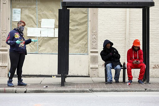 In this Tuesday, March 24, 2020 photo, Sabrina Dockery, left, waits for the bus wearing protective gear in Cincinnati, on the first day of Ohio Gov. Mike DeWine's shelter-in-place order in response to the new coronavirus pandemic. All non-essential businesses are closed and residents have been asked to stay at home. (Kareem Elgazzar/The Cincinnati Enquirer via AP)