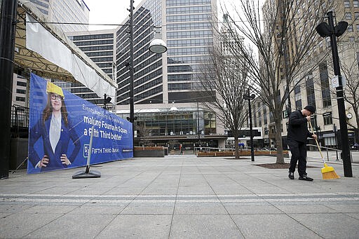 In this Tuesday, March 24, 2020 photo, Chris Klenk, a 3CDC operations supervisor, sweeps at Fountain Square in Cincinnati, on the first day of Ohio Gov. Mike DeWine's shelter-in-place order in response to the new coronavirus pandemic. All non-essential businesses are closed and residents have been asked to stay at home. (Kareem Elgazzar/The Cincinnati Enquirer via AP)