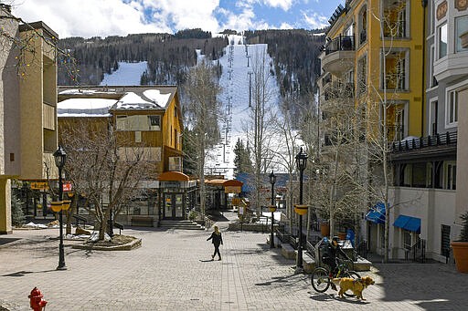 This Tuesday, March 24, 2020 photo shows people walking through empty streets at the base of Vail Ski Resort after the resort closed for the season amid the COVID-19 pandemic, in Vail, Colo. Ski resorts across the West that were shut down amid coronavirus fears are grappling with an economic blow at a time they would normally be welcoming hordes of spring break revelers.  (AP Photo/Michael Ciaglo)