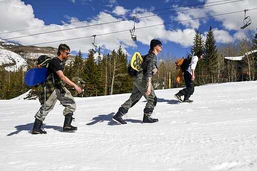 This Tuesday, March 24, 2020 photo shows snowboarders, from left, Colin Tabb, Tyler Alvarez and Shaun Carroll, determined to get in a run, hike up an empty ski run past a closed chair lift at Vail, Colo., after Vail Ski Resort closed for the season amid the COVID-19 pandemic. &#147;Today it&#146;s desolate. It&#146;s a ghost town,&quot; said Tabb, a Vail resident and snowboarder. &#147;Usually we are fighting lift lines and we are doing our thing still, but it&#146;s a complete ghost town.&#148; (AP Photo/Michael Ciaglo)