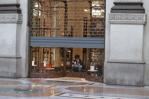 FILE - In this Wednesday, March 11, 2020 filer, a cleaner sits in a shut down shop at the Vittorio Emanuele shopping arcade in Milan, Italy. The eurozone's third-largest economy and a major exporter, Italy on Wednesday becomes the first western industrialized nation to idle swaths of industrial production to stop the spread of coronavirus by keeping yet more of the population at home. The new coronavirus causes mild or moderate symptoms for most people, but for some, especially older adults and people with existing health problems, it can cause more severe illness or death. (AP Photo/Luca Bruno, File)