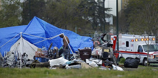 In this March 19, 2020 file photo, an ambulance drives by a homeless encampment in Oakland, Calif. Efforts to move California's large homeless population into isolated quarters to slow the spread of the coronavirus are still sluggish despite a $150 million cash infusion by the governor and a crisis that public health experts say needs to be curbed now. (AP Photo/Ben Margot)