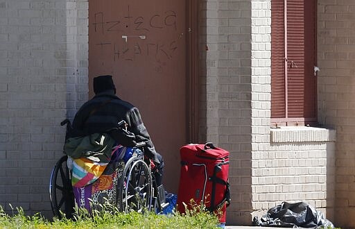 A man sits in a wheelchair as he joins crowds along sidewalks where many homeless people live along the streets, as concerns grow over the homeless population due to the coronavirus Tuesday, March 24, 2020, in Phoenix. (AP Photo/Ross D. Franklin)