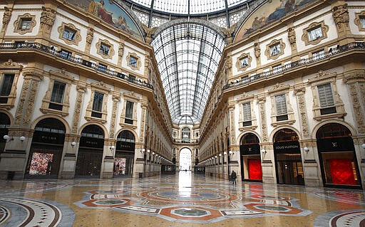 FILE - In this Sunday, March 22, 2020 filer, a man walks in an empty Vittorio Emanuele II gallery shopping arcade, in downtown Milan, Italy. The eurozone's third-largest economy and a major exporter, Italy on Wednesday becomes the first western industrialized nation to idle swaths of industrial production to stop the spread of coronavirus by keeping yet more of the population at home. The new coronavirus causes mild or moderate symptoms for most people, but for some, especially older adults and people with existing health problems, it can cause more severe illness or death. (AP Photo/Antonio Calanni, File)