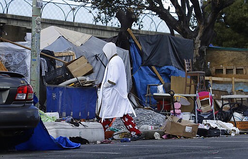 A man walks through a homeless encampment on Wednesday, March 25, 2020, in Oakland, Calif. Efforts to move California's large homeless population into isolated quarters to slow the spread of the coronavirus are still sluggish despite a $150 million cash infusion by the governor and a crisis that public health experts say needs to be curbed now.   (AP Photo/Ben Margot)