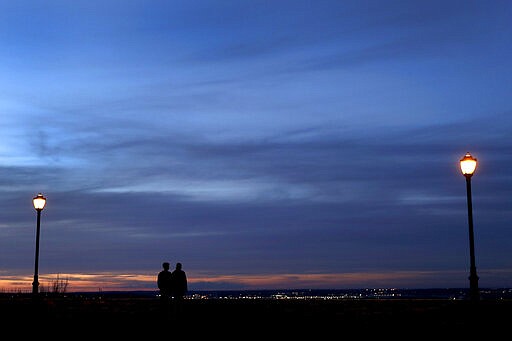 A couple watch the sun set, Wednesday, March 25, 2020, in Kansas City, Mo. The city, along with neighboring counties, is under Stay at Home orders to help prevent the spread of COVID-19, the disease caused by the new coronavirus. (AP Photo/Charlie Riedel)