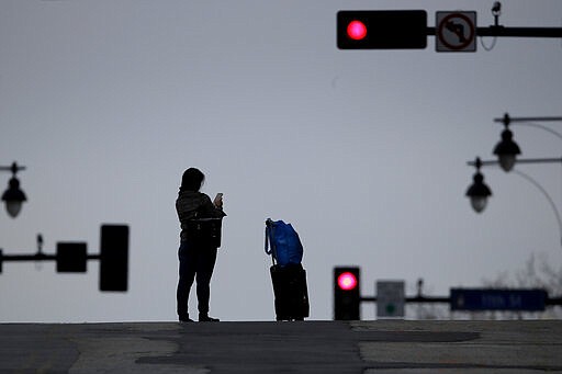 A pauses in the middle of an empty downtown street to look at her phone Tuesday, March 24, 2020 on the first day of a stay-at-home order in Kansas City, Mo. Kansas City and surrounding counties instituted a 30-day mandatory stay-at-home order in an effort to stem the spread of the coronavirus. (AP Photo/Charlie Riedel)