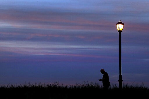 A man walks in a park at dusk, Wednesday, March 25, 2020, in Kansas City, Mo. The city, along with neighboring counties, is under Stay at Home orders to help prevent the spread of COVID-19, the disease caused by the new coronavirus. (AP Photo/Charlie Riedel)