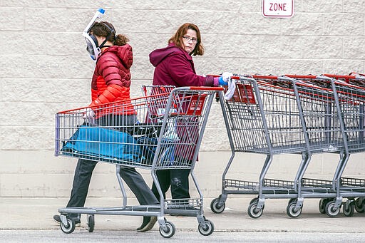 A Costco employee, right, looks towards a shopper wearing a mask and snorkel to go shopping, as she sanitizes carts that are returned from the parking lot to help reduce the spread of coronavirus, in King of Prussia, Pa., Wednesday, March 25, 2020. (Michael Bryant/The Philadelphia Inquirer via AP)