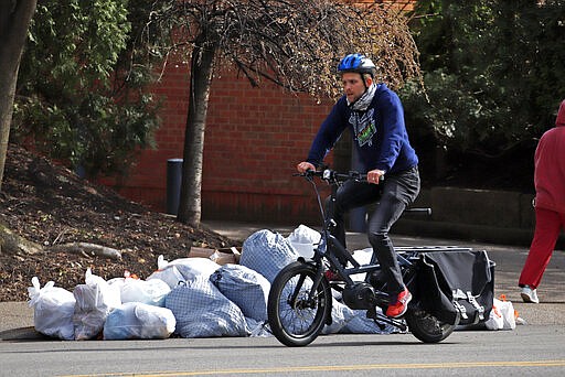 A bicyclist rides past a pile of trash in the Oakland section of Pittsburgh, Wednesday, March 25, 2020. Wednesday morning sanitation workers refused to collect the regularly scheduled trash pickup, expressing concerns that there were not enough safety measures in place to protect workers from potential exposure to COVID-19. The workers demanded protective equipment and hazard pay. The city anticipates normal garbage pickup to resume on Thursday. (AP Photo/Gene J. Puskar)