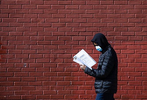 Terrell Bell, wearing a protective face mask, looks at a learning guide he picked up for his little sister at John H. Webster Elementary School in Philadelphia, Thursday, March 26, 2020. Gov. Tom Wolf&#146;s administration reported more new coronavirus-related deaths in Pennsylvania on Wednesday. Residents are ordered to stay home, with few exceptions. (AP Photo/Matt Rourke)