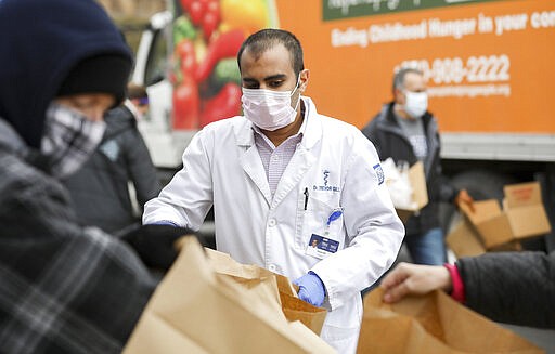 Wright Center resident Dr. Trevor Gill packs bags of food during the COVID-19 Emergency Drive-Through Food Giveaway hosted by The Wright Center for Community Health, Friends of the Poor, Family to Family Food Basket Program, the Commission on Economic Opportunity, and the Weinberg Northeast Regional Food Bank in Jermyn, Pa., on Wednesday, March 25, 2020. (Jake Danna Stevens/The Times-Tribune via AP)