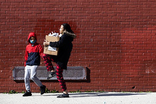 A woman carries a box of donated food and educational materials that she picked up at John H. Webster Elementary School in Philadelphia, Thursday, March 26, 2020. Gov. Tom Wolf&#146;s administration reported more new coronavirus-related deaths in Pennsylvania on Wednesday. Residents are ordered to stay home, with few exceptions. (AP Photo/Matt Rourke)