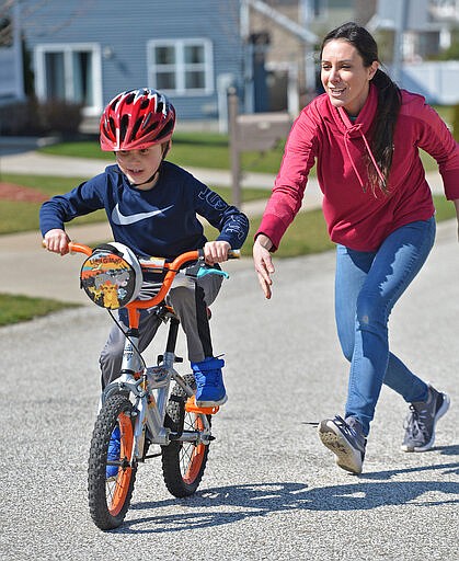 Cameron Mezzacapo, 7, gets a push from his mother, Milynn Mezzacapo, while learning to ride a bike, Wednesday, March 25, 2020, near their home in the Evergreen Farms development in Fairview Township, Pa. Milynn Mezzacapo said the extra time at home motivated them. &quot;We finally have the time and the weather is nice,&quot; she said. (Christopher Millette/Erie Times-News via AP)