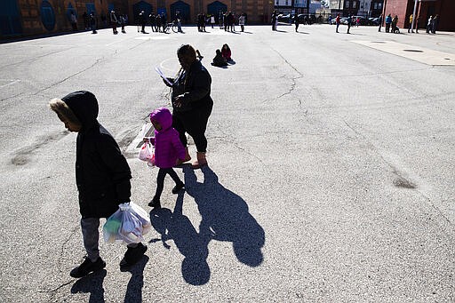 A woman and children walk away from the John H. Webster Elementary School carrying donated food and educational materials, in Philadelphia, Thursday, March 26, 2020. Gov. Tom Wolf&#146;s administration reported more coronavirus-related deaths in Pennsylvania on Wednesday. Residents are ordered to stay home, with few exceptions. (AP Photo/Matt Rourke)