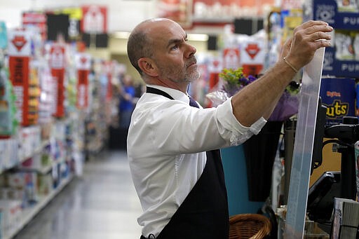 Dave Herrick installs a plexiglass panel at a checkout lane at a Hy-Vee grocery store Thursday, March 26, 2020 in Overland Park, Kan. Stores have begun installing plexiglass shields in the checkout aisles as a precaution to protect clerks and help stop the spread the new coronavirus. (AP Photo/Charlie Riedel)