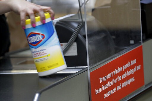 A clerk scans a can of sanitizing wipes as she checks out groceries behind a plexiglass panel at a Hy-Vee grocery store Thursday, March 26, 2020 in Overland Park, Kan. Stores have begun installing the shields in checkout aisles as a precaution to protect clerks and help stop the spread the new coronavirus. (AP Photo/Charlie Riedel)