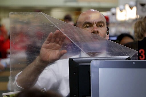 Dave Herrick installs a plexiglass panel at a checkout lane at a Hy-Vee grocery store Thursday, March 26, 2020 in Overland Park, Kan. Stores have begun installing plexiglass shields in the checkout aisles as a precaution to protect clerks and help stop the spread the new coronavirus. (AP Photo/Charlie Riedel)