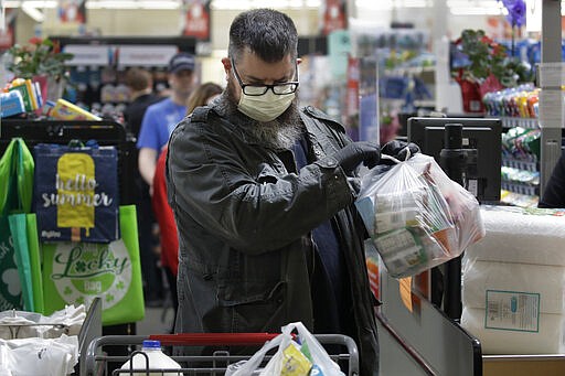 A man gathers his groceries after checking out at a Hy-Vee grocery store Thursday, March 26, 2020 in Overland Park, Kan. Stores have begun installing plexiglass shields in checkout aisles as a precaution to protect clerks and help stop the spread the new coronavirus. (AP Photo/Charlie Riedel)