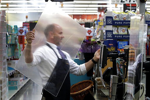 Dave Herrick installs a plexiglass panel at a checkout lane at a Hy-Vee grocery store Thursday, March 26, 2020 in Overland Park, Kan. Stores have begun installing plexiglass shields in the checkout aisles as a precaution to protect clerks and help stop the spread the new coronavirus. (AP Photo/Charlie Riedel)