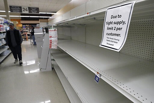 A passer-by walks down an aisle with empty shelves where paper towels are normally on display at a grocery store, Thursday, March 26, 2020, in Quincy, Mass. Paper towels and toilet paper have sold briskly as people take measures to cope with the coronavirus. The new coronavirus causes mild or moderate symptoms for most people, but for some, especially older adults and people with existing health problems, it can cause more severe illness or death. (AP Photo/Steven Senne)