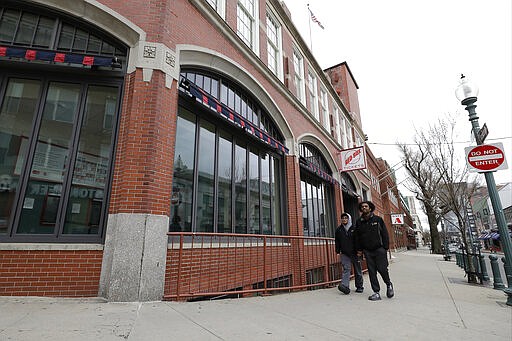 Passers-by walk past Fenway Park baseball park, Wednesday, March 25, 2020, in Boston. There will be empty ballparks on what was supposed to be Major League Baseball's opening day, with the start of the Major League Baseball regular season indefinitely on hold because of the coronavirus pandemic. (AP Photo/Steven Senne)