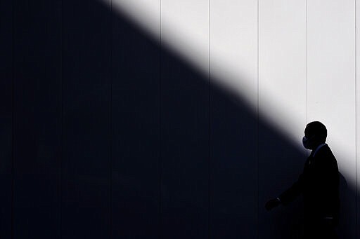 A man wearing a mask is silhouetted against a wall as he walks into the shade of a building Thursday, March 26, 2020, in Tokyo. Japan's Prime Minister Shinzo Abe is setting up a special task force to discuss coronavirus measures and emergency responses as the government now considers the spread of the COVID-19 virus rampant in the country, officials said Thursday. (AP Photo/Jae C. Hong)