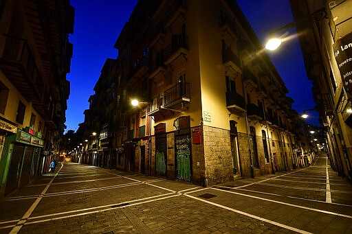 A pedestrian walks near to the corner between Estafeta, left, and Javier street of the old city, in Pamplona, northern Spain, Wednesday, March 25, 2020. The new coronavirus causes mild or moderate symptoms for most people, but for some, especially older adults and people with existing health problems, it can cause more severe illness or death. (AP Photo/Alvaro Barrientos)