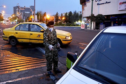 A Revolutionary Guard member disinfects a car to help prevent the spread of the new coronavirus in downtown Tehran, Iran, Wednesday, March 25, 2020.  Iran is battling the worst outbreak in the region and authorities have advised people to stay at home but have not imposed the kinds of lockdowns seen elsewhere. (AP Photo/Ebrahim Noroozi)