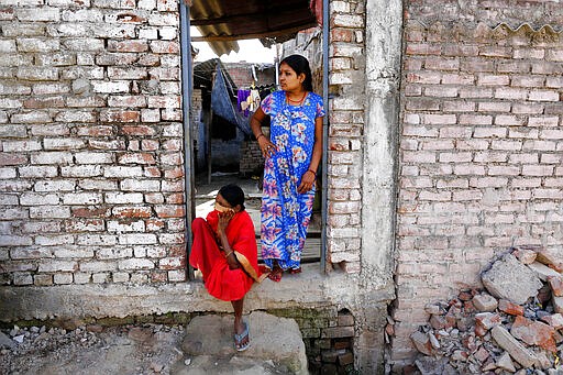 Women look out a door in a neighborhood mostly inhabited by daily wage laborers in Prayagraj, India , Thursday, March 26, 2020. Some of India's legions of poor and people suddenly thrown out of work by a nationwide stay-at-home order began receiving aid distribution Thursday, as both the public and private sector work to blunt the impact of efforts to curb the coronavirus pandemic. Untold numbers of them are now out of work and many families have been left struggling to eat. (AP Photo/Rajesh Kumar Singh)