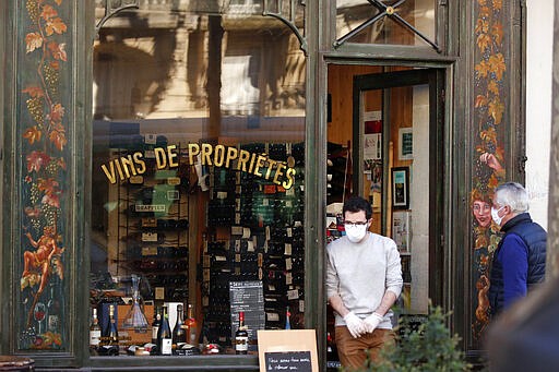 Parisian wearing protective masks stand in front of a wine shop in Paris, Tuesday, March 24, 2020. French President Emmanuel Macron urged employees to keep working in supermarkets, production sites and other businesses that need to keep running amid stringent restrictions of movement due to the rapid spreading of the new coronavirus in the country. For most people, the new coronavirus causes only mild or moderate symptoms. For some it can cause more severe illness, especially in older adults and people with existing health problems. (AP Photo/Francois Mori)