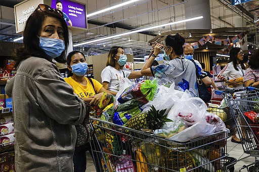 Shoppers wearing face masks with a cart full of food supplies wait in line to pay at a supermarket counter in Singapore, Tuesday, Mar. 17, 2020. Singaporeans were seen buying food supplies in supermarkets following neighboring Malaysia's announcement of a nationwide lockdown from the coronavirus to begin Wednesday which could affect the flow of food supplies to the city state. (AP Photo/Ee Ming Toh)