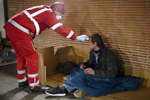 A red cross volunteer checks the temperature of a homeless man, in Rome, Wednesday, March 25, 2020. The new coronavirus causes mild or moderate symptoms for most people, but for some, especially older adults and people with existing health problems, it can cause more severe illness or death. (AP Photo/Andrew Medichini)