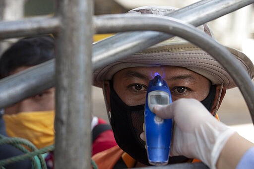 A health officer checks the temperature of a passenger in truck at a health check point in Bangkok, Thailand, Thursday, March 26, 2020. The country is on the first day of month long state of emergency enforced to allow its government to impose stricter measures to control the coronavirus that has infected hundreds of people in the Southeast Asian country. (AP Photo/Sakchai Lalit)