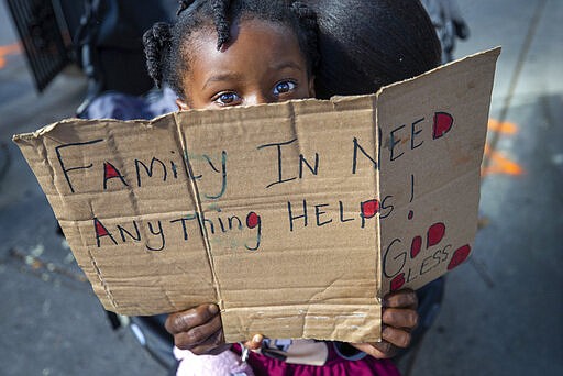 Nyla Clark, 3, accompanied by her mother, Chavonne Clark, sits in a baby stroller at a corner in New Orleans, hoping to get a few dollars from an occasional passerby Wednesday, March 25, 2020. Clark was a phlebotomist with a local company until she lost her job because of the coronavirus pandemic. She is waiting for unemployment. (David Grunfeld/The Advocate via AP)