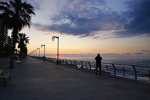 In this Saturday, March 21, 2020 photo, a man takes pictures of the sunset on Beirut's Mediterranean seaside corniche, which is almost empty of residents and tourists in Beirut, Lebanon. The COVID-19 pandemic has managed to do what various wars could not: Close bars, restaurants and entertainment spots across the tiny Mediterranean country. Even Lebanon's corniche, usually dotted with people doing their morning exercise, coffee vans and corn on the cob sellers, is now empty. (AP Photo/Bilal Hussein)